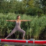 Woman performing yoga pose on paddleboard in calm lake, surrounded by nature